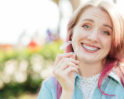 Dental care.Smiling girl with braces on her teeth holds aligners in her hands and shows the difference between them